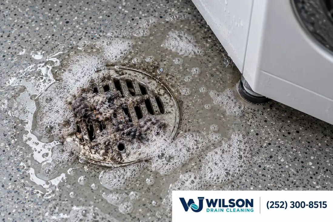Before view: Utility laundry floor drain on speckled gray floor beside washing machine foot.